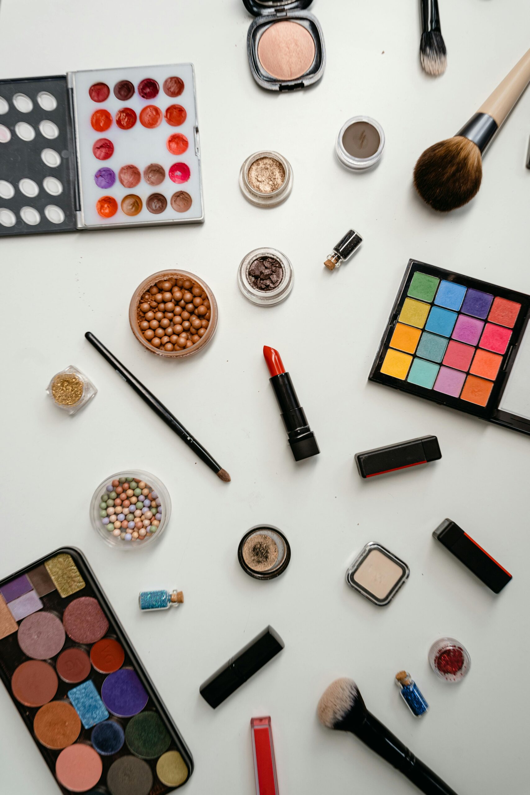 Top view of a multicolored makeup assortment featuring eyeshadow palettes, brushes, and lipsticks.
